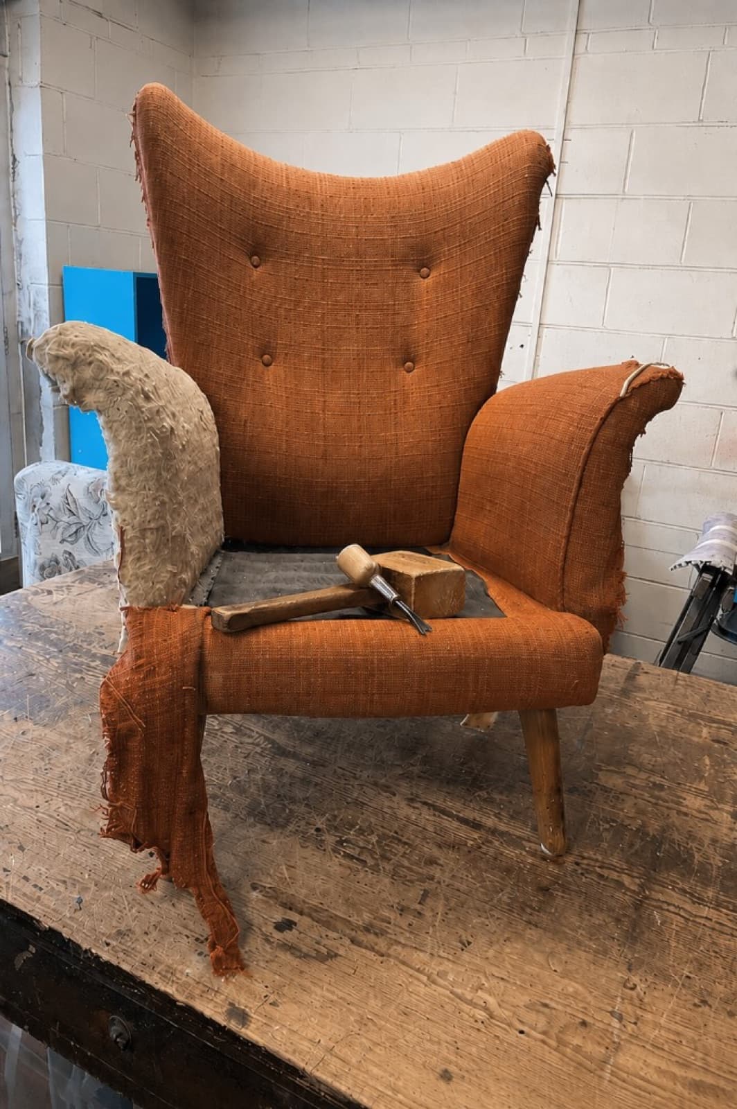 Worn orange wingback armchair mid-strip on the workshop bench