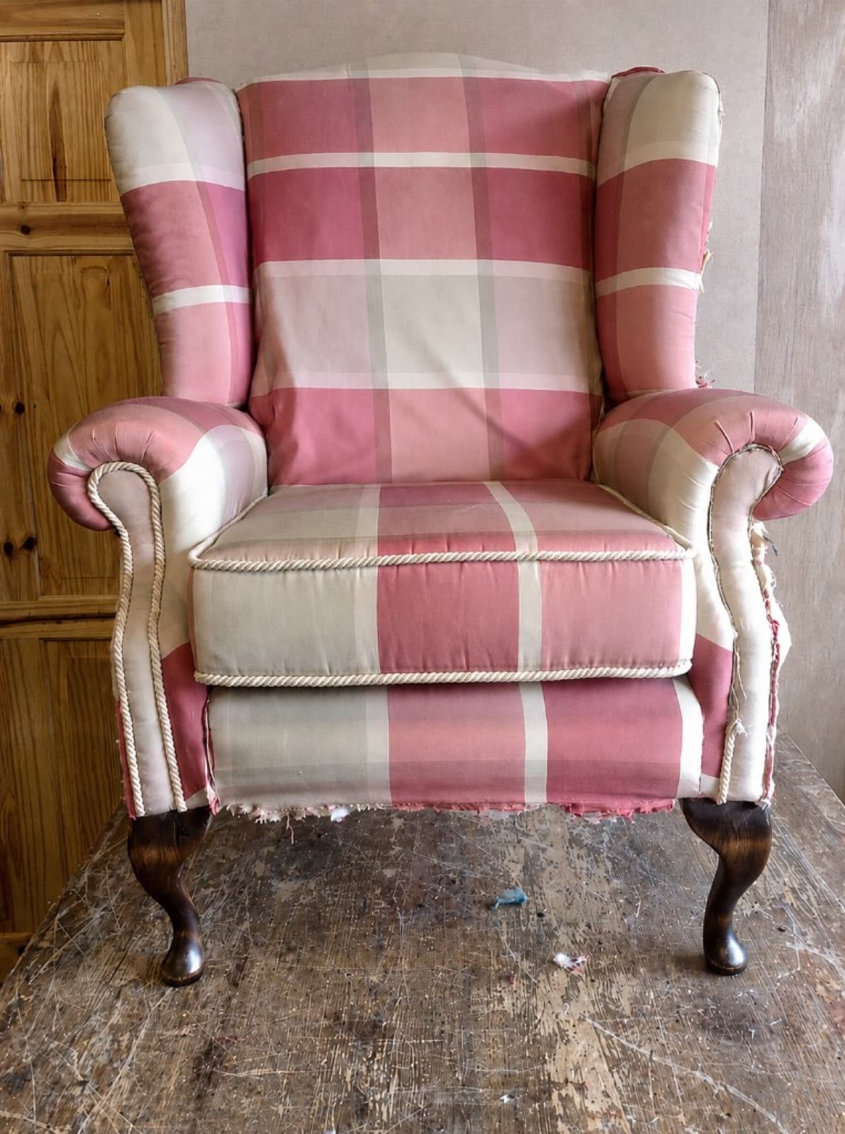 Worn wingback armchair in pink and cream plaid fabric before reupholstery