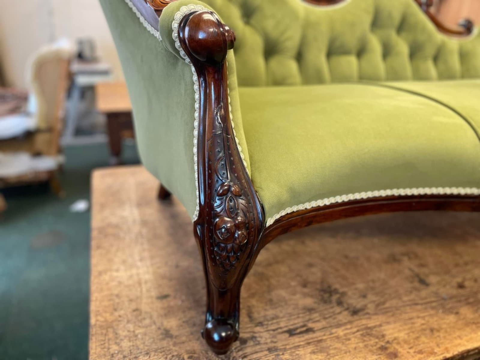 Close detail of olive green velvet sofa with carved wood and cream gimp trim