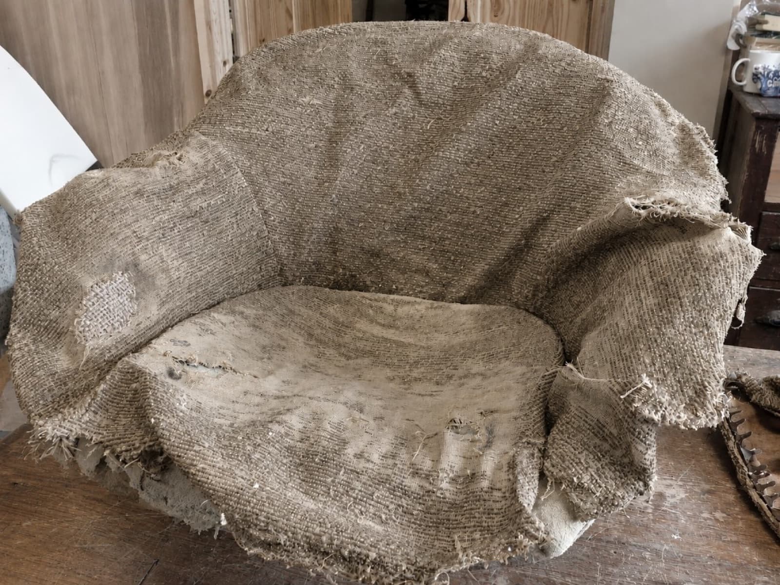 Worn tub armchair stripped to frayed hessian before reupholstery