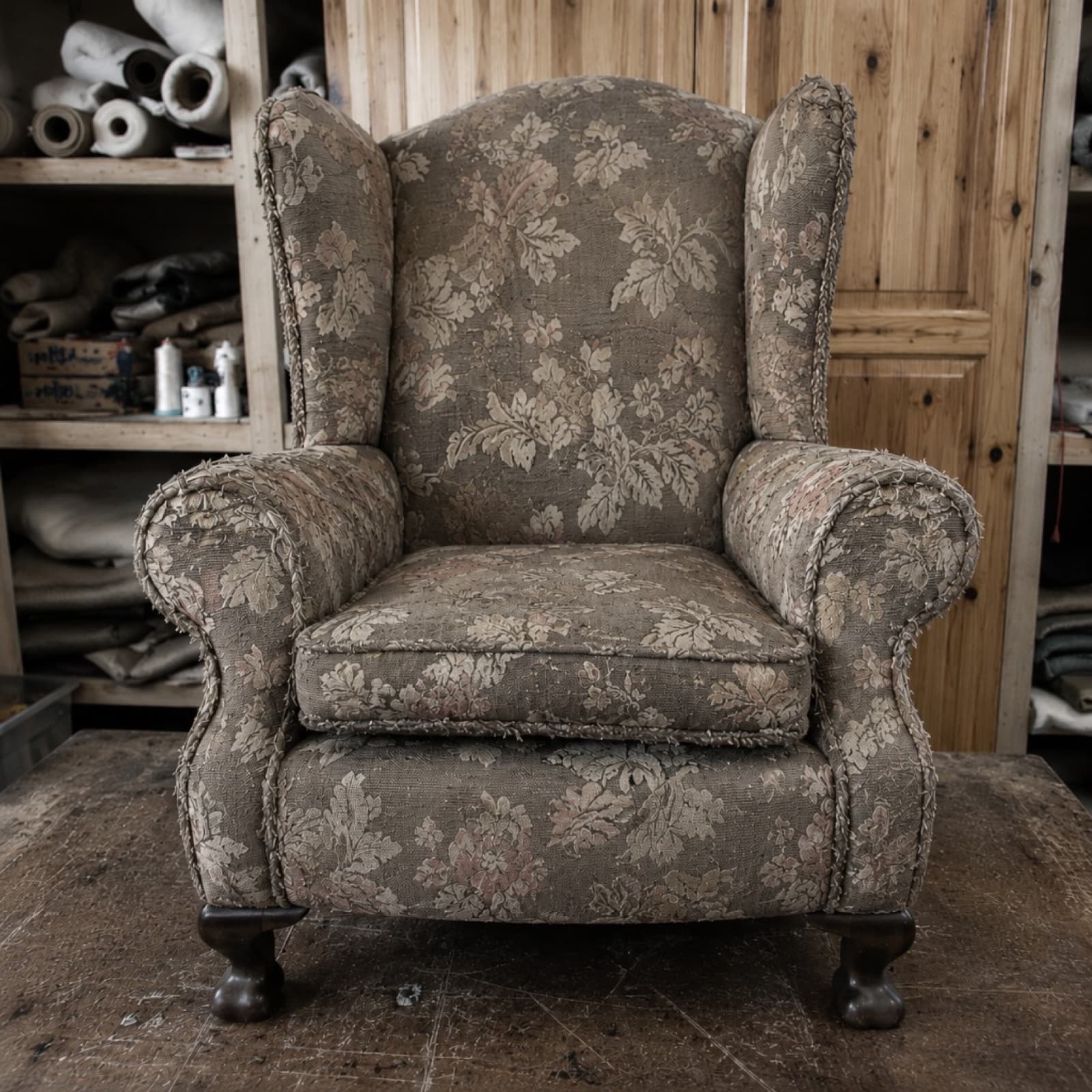 Worn wingback armchair in faded taupe floral fabric before reupholstery